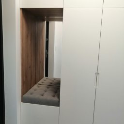 JMM PROJEKT Michał Marciniak - Biała szafa wnękowa z siedziskiem z szarej tapicerki z guzikami, drewniane wykończenie wnęki, minimalistyczny design.