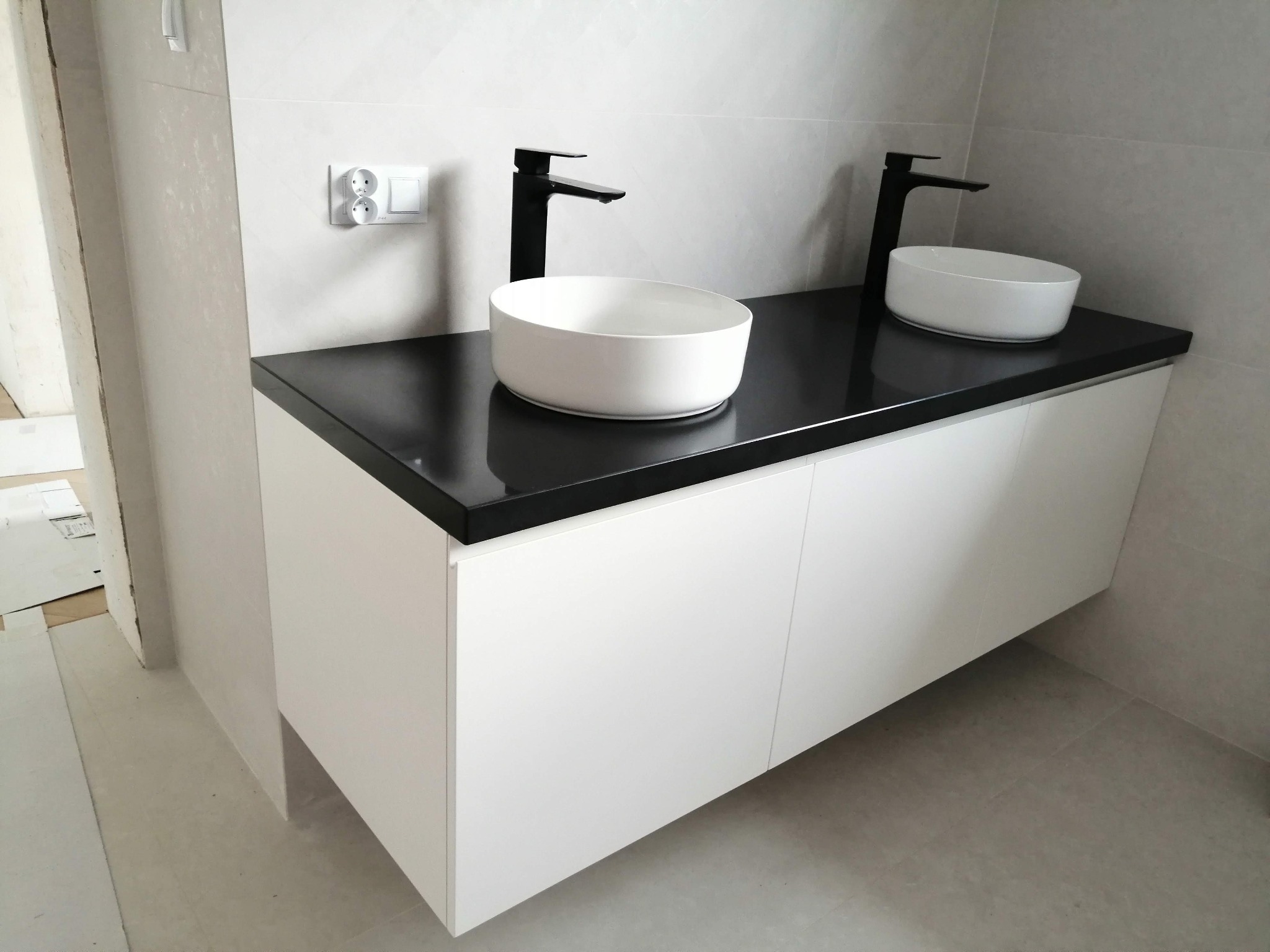 Nowoczesna łazienka z białą szafką podumywalkową z czarnym blatem, na którym stoją dwie okrągłe, białe umywalki i czarne baterie.