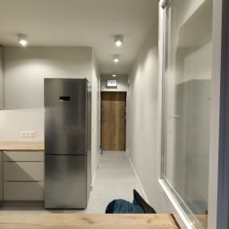 Marcin Oblak - Wnętrze mieszkania po remoncie: widok na korytarz z nową podłogą, świeżo pomalowane ściany i sufit z zamontowanym oświetleniem punktowym. W tle widoczne drzwi wejściowe. Na pierwszym planie...