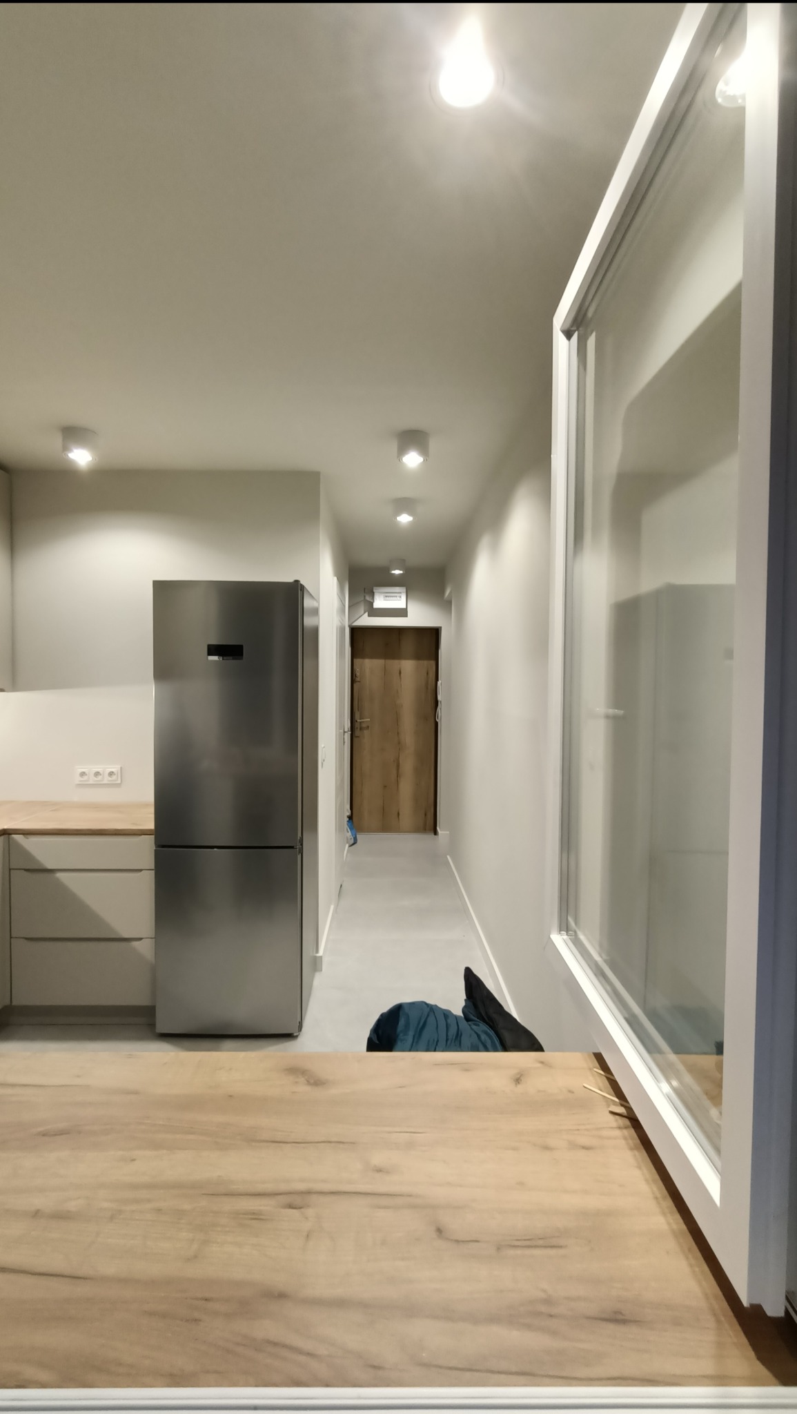 Wnętrze mieszkania po remoncie: widok na korytarz z nową podłogą, świeżo pomalowane ściany i sufit z zamontowanym oświetleniem punktowym. W tle widoczne drzwi wejściowe. Na pierwszym planie...