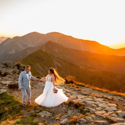 Lovegrafia MARTYNA JODŁOWSKA - Para młoda w Zatorze na tle gór o zachodzie słońca. Panna młoda w białej sukni, pan młody w szarym garniturze. Kamienista ścieżka i ciepłe światło.