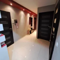 Jasny korytarz po remoncie z białymi płytkami na podłodze, ciemnymi drzwiami z poziomymi przeszkleniami i szarą ścianą z dekoracyjnym pasem w kolorze bordo pod sufitem.