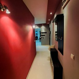 Karol Bubak - Pomalowany na czerwono korytarz z błyszczącą podłogą, oświetlony lampami ściennymi i punktowymi, z czarnymi meblami wzdłuż ściany i widokiem na dalsze pomieszczenia.