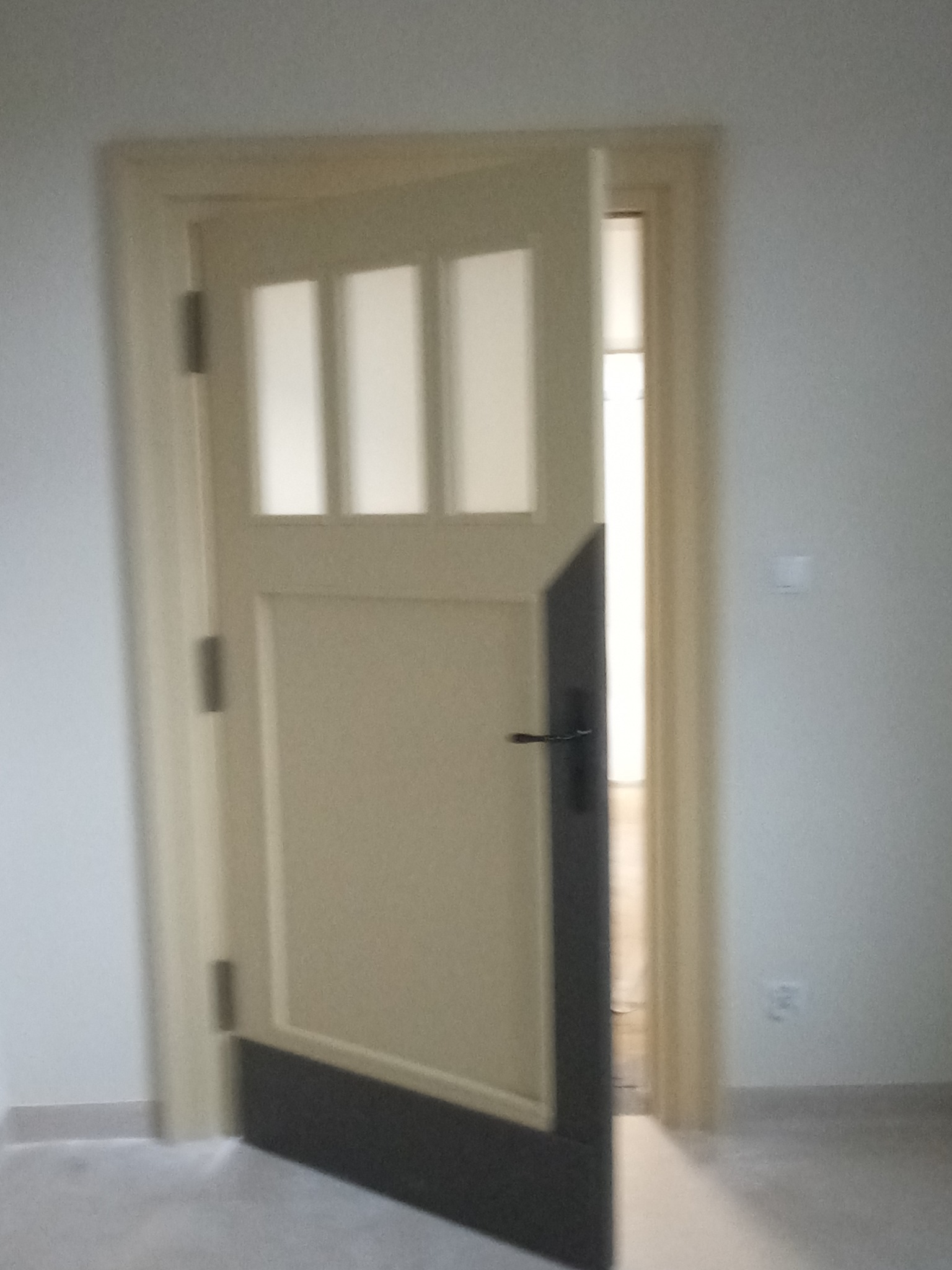 Otwarta, częściowo przeszklona, beżowa konstrukcja z ciemnym dołem i czarną klamką, widok na jasne pomieszczenie w tle.