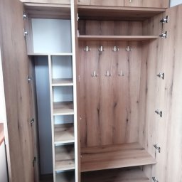 RKMeble - Rafał Kolbusz - Otwarta szafa wnękowa z jasnego drewna z półkami i wieszakami, widoczne zawiasy i podział na strefy.