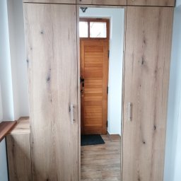 RKMeble - Rafał Kolbusz - Szafa wnękowa z lustrem na środkowych drzwiach, odbijająca drewniane drzwi wejściowe z szybką, widoczna faktura drewna na frontach szafy.