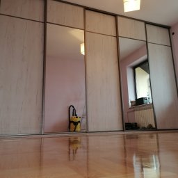 RKMeble - Rafał Kolbusz - Duża szafa wnękowa z przesuwnymi drzwiami i lustrami, na podłodze widoczny odkurzacz przemysłowy.