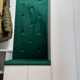 Wnęka z siedziskiem tapicerowanym zielonym welurem z guzikami, wkomponowana w szafę w Sędziszowie Małopolskim. Obok wieszak z kurtką.