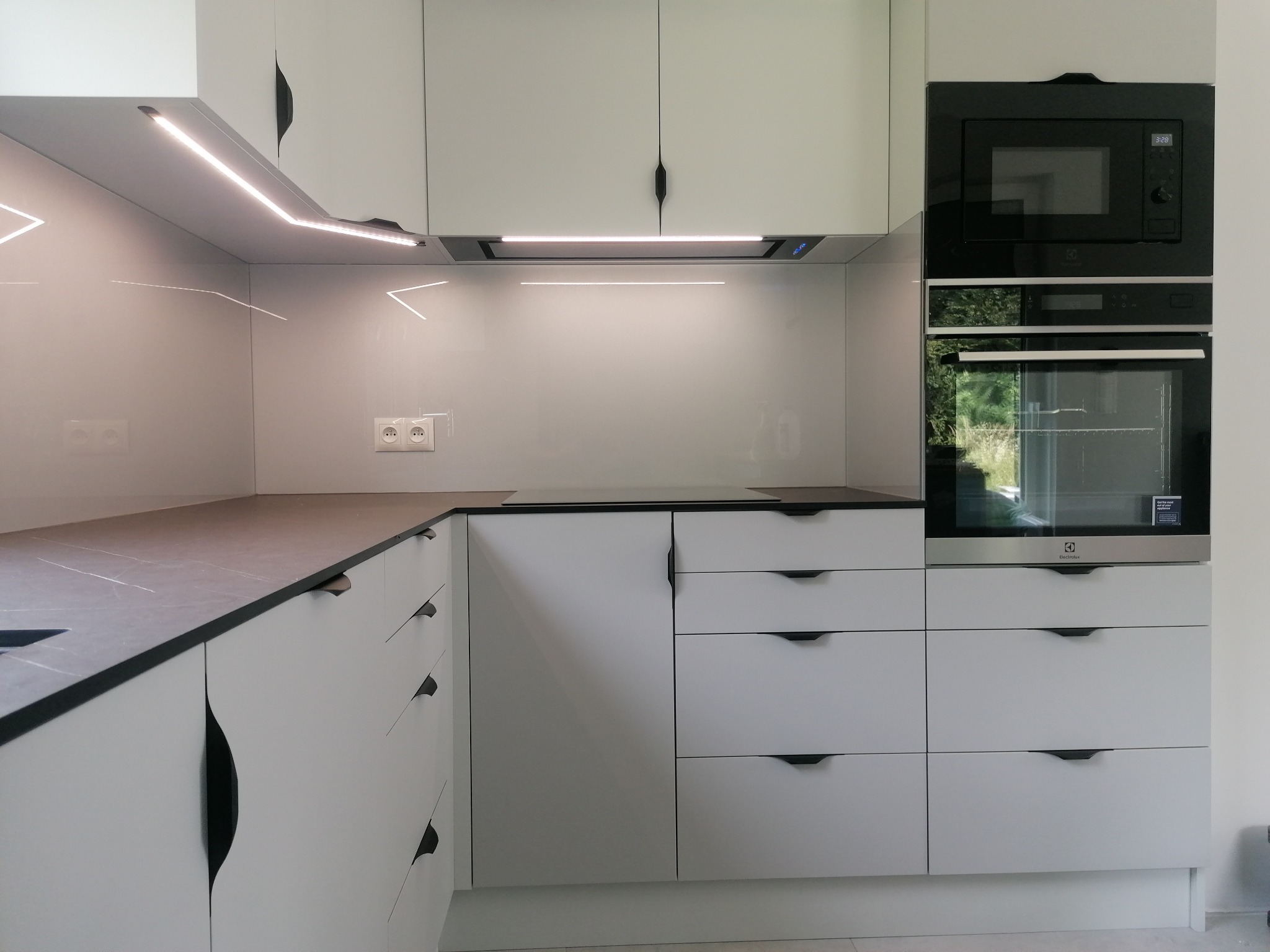 Nowoczesna, jasna kuchnia z szarym blatem i zabudowanymi sprzętami AGD, oświetlenie LED pod szafkami górnymi.