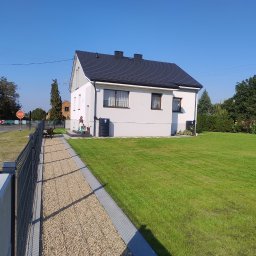 Eko Płot Systemy Ogrodzeniowe Krzysztof Łasiński - Nowoczesny dom z szarego metalowego ogrodzenia panelowego z podmurówką, widok z zewnątrz na posesję z trawnikiem i ścieżką z kamyków.