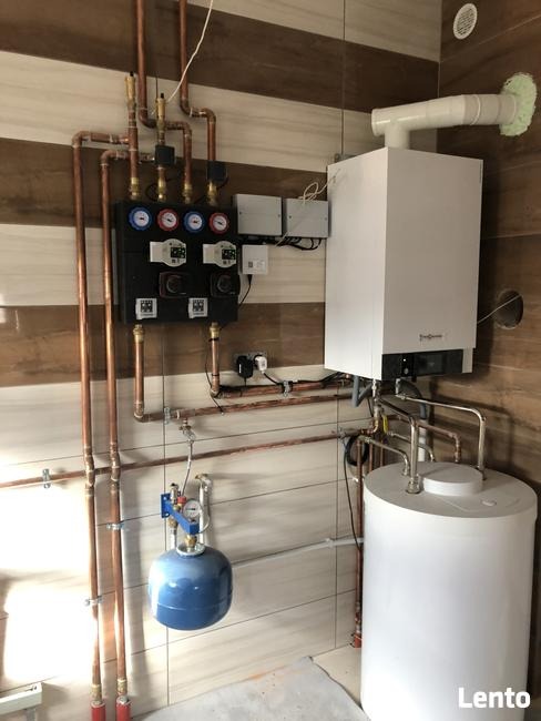 Nowoczesny piec gazowy Viessmann z osprzętem i niebieskim zbiornikiem wyrównawczym, zamontowany w kotłowni w Małkowie, z widocznymi miedzianymi rurami instalacji grzewczej.