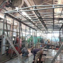 GSM SPÓŁKA Z OGRANICZONĄ ODPOWIEDZIALNOŚCIĄ - Spawanie konstrukcji metalowej w hali produkcyjnej we Wrocławiu, widoczne iskry, spawacze w kombinezonach oraz szkielet konstrukcji.