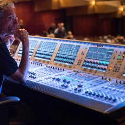 VLVV HOLDINGS - Operator dźwięku w Katowicach, zamyślony, siedzi przed dużą konsolą mikserską Soundcraft Vi6 podczas wydarzenia na żywo, w tle widoczna publiczność.