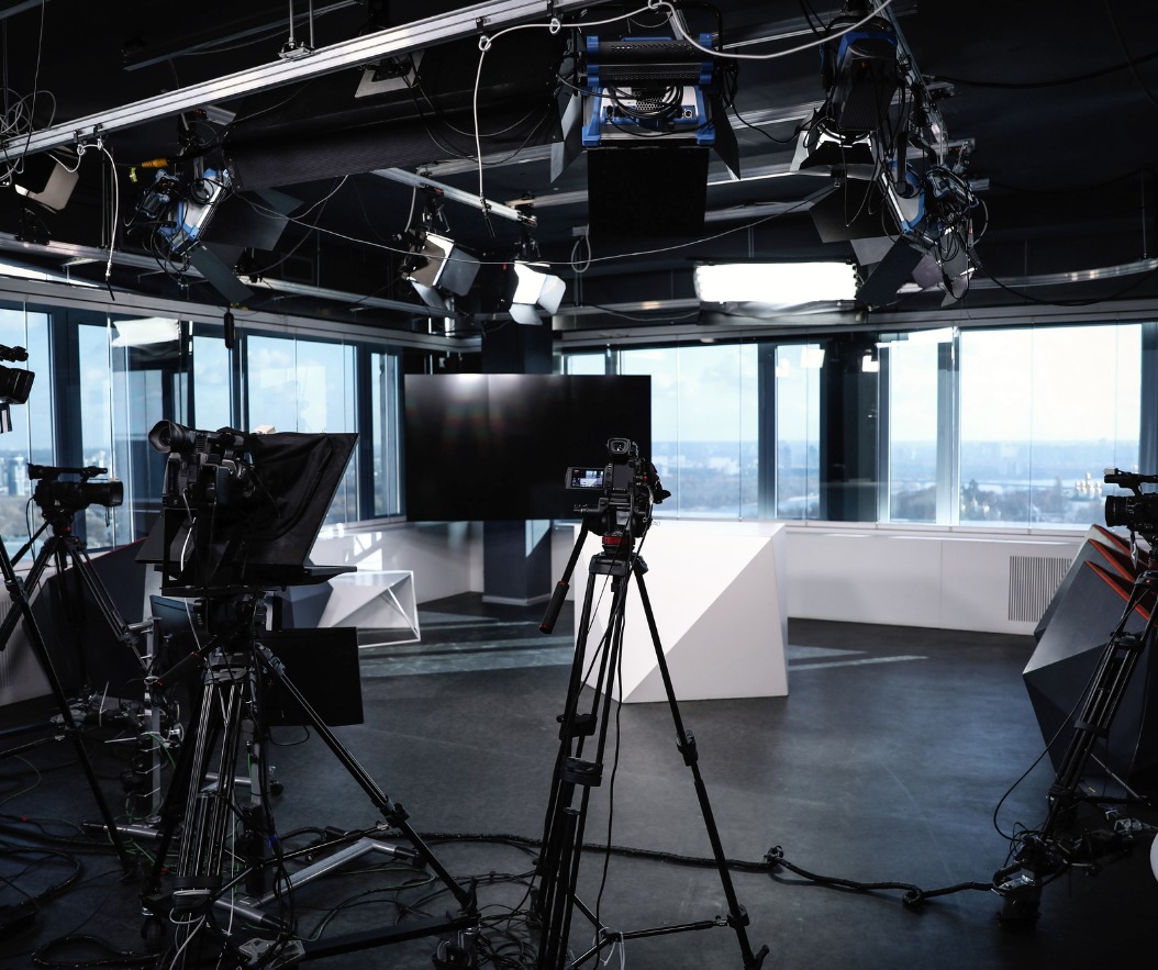 Studio filmowe z trzema kamerami na statywach, oświetleniem sufitowym i dużym oknem z widokiem na miasto w tle.