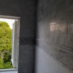 Ściana wyłożona marmurowymi płytkami z dekoracyjną listwą, widok na otwarte okno z zielenią na zewnątrz.