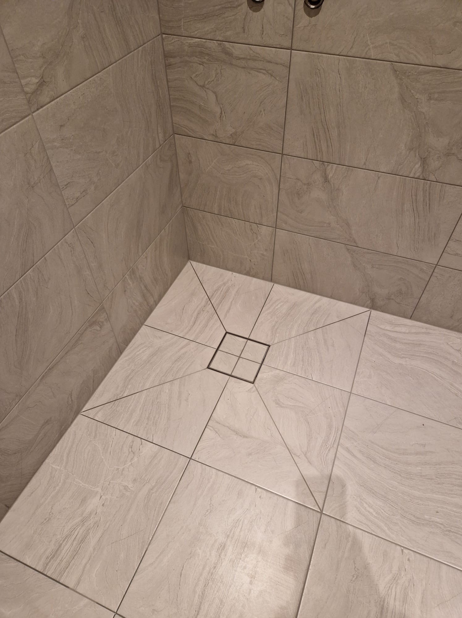 Wykończona kabina prysznicowa z szarymi płytkami imitującymi kamień, odpływ liniowy w kształcie kwadratu z cienką ramką.