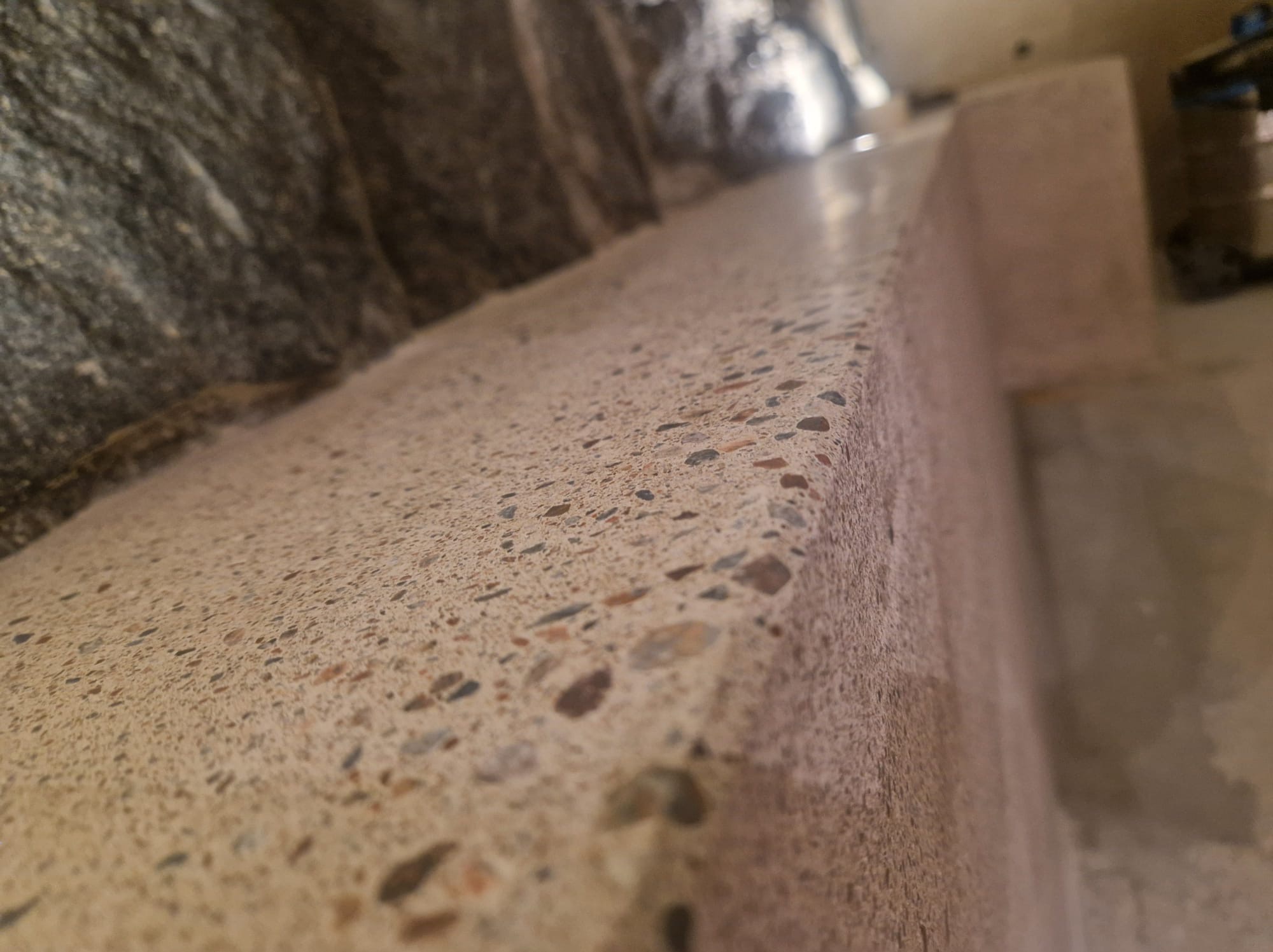 Szlifowana posadzka z lastryko z widocznymi kamyczkami, przy ścianie wyłożonej kamieniem naturalnym, perspektywa z dołu.