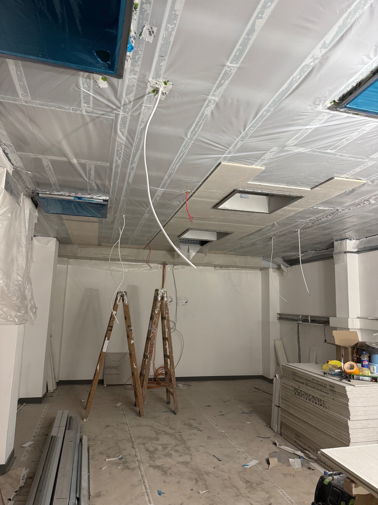 Wnętrze w trakcie montażu sufitu podwieszanego z płyt kartonowo-gipsowych, widoczne profile, drabina malarska i zabezpieczona folią przestrzeń pod sufitem.