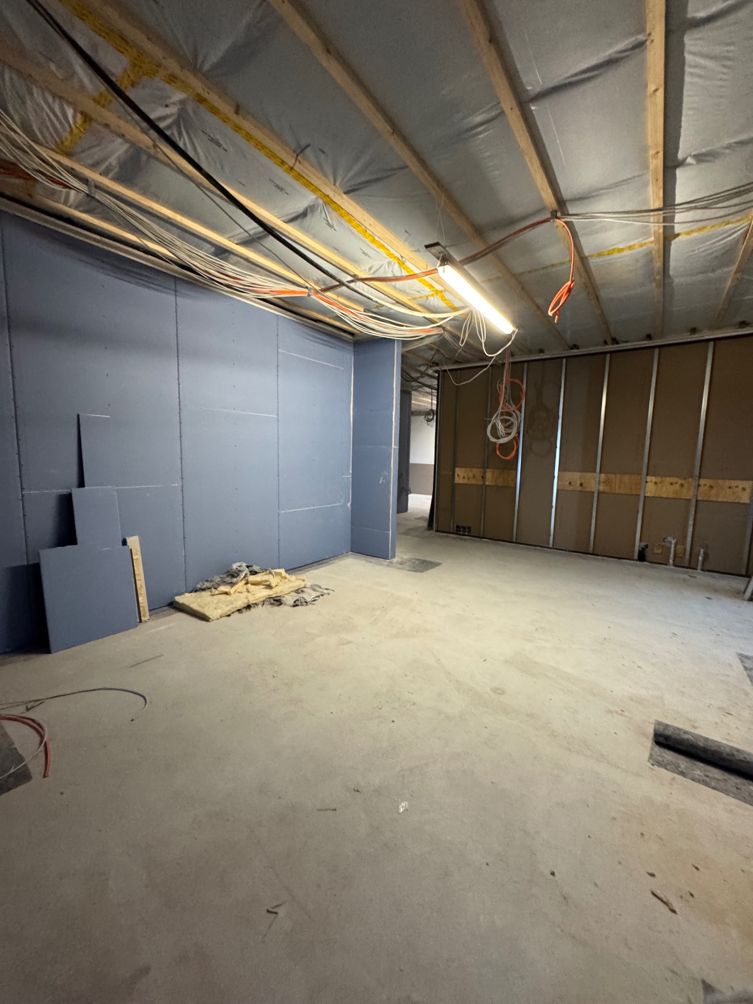 Wnętrze w trakcie prac wykończeniowych: ściany obłożone płytami kartonowo-gipsowymi, widoczne przewody elektryczne pod sufitem i fragmenty izolacji na podłodze.
