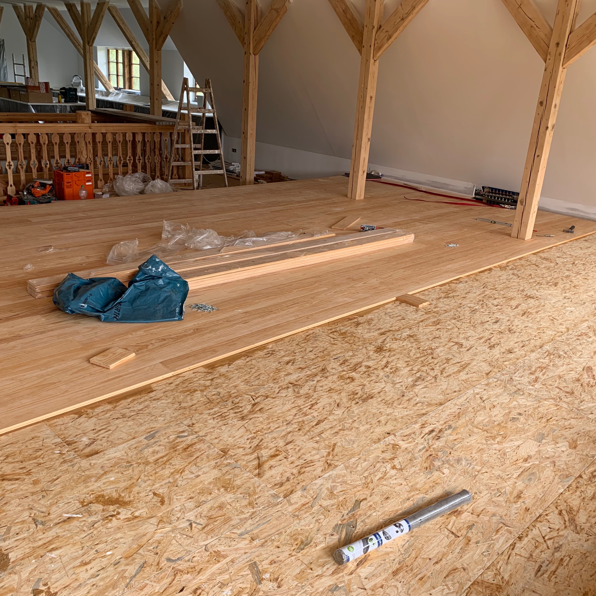 Poddasze w trakcie układania drewnianej podłogi na płycie OSB; widoczne deski podłogowe, narzędzia i materiały budowlane.
