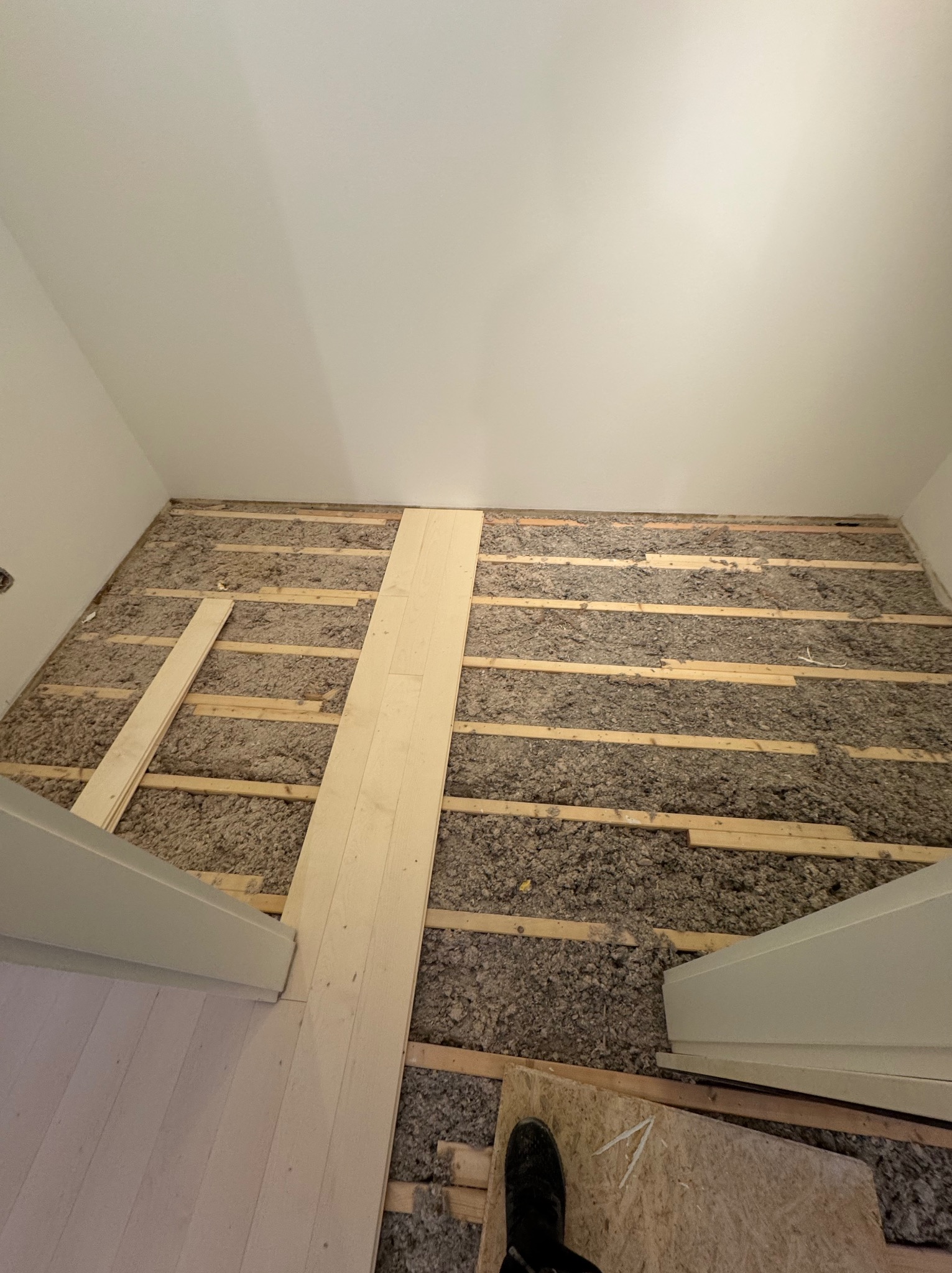 Ocieplenie podłogi wełną mineralną między legarami, częściowo zakryte deskami. Widok z góry na poddasze lub strych w trakcie prac wykończeniowych.