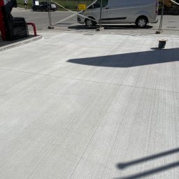 FA MATLAG MATLĄG STANISŁAW - Świeżo wykonana, szara posadzka przemysłowa z widocznymi nacięciami dylatacyjnymi. W tle dystrybutory paliw i zaparkowany bus.