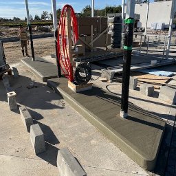 FA MATLAG MATLĄG STANISŁAW - Świeżo wykonana, gładka wylewka pod zadaszeniem, z widocznymi elementami konstrukcyjnymi i narzędziami pracy. W tle widoczny pracownik i teren budowy.