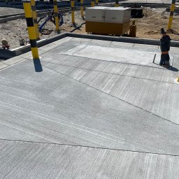 FA MATLAG MATLĄG STANISŁAW - Szara, gładka powierzchnia z betonu podzielona na segmenty, z widocznym odpływem i słupkami ostrzegawczymi w tle. Prace wykończeniowe w przestrzeni publicznej.