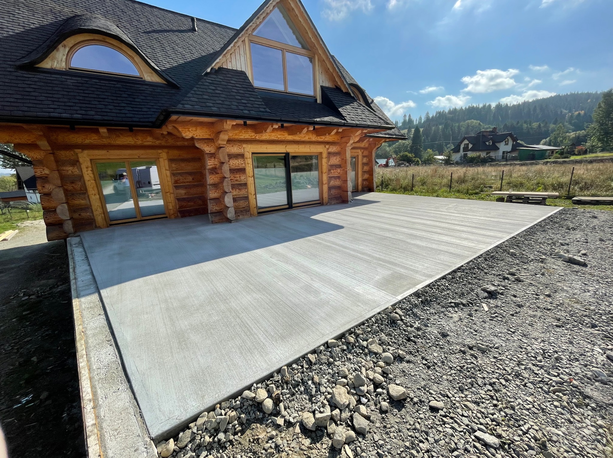 Nowa, gładka wylewka tarasu przy drewnianym domu w górskim stylu. Widok na góry w tle, słoneczny dzień.