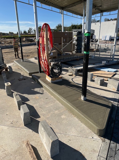 Świeżo wykonana, gładka wylewka pod zadaszeniem, z widocznymi elementami konstrukcyjnymi i narzędziami pracy. W tle widoczny pracownik i teren budowy.