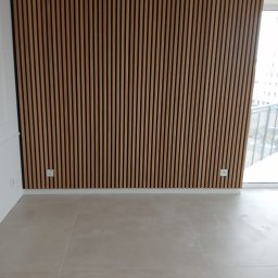 Paweł Żoch - Ściana z drewnianych paneli akustycznych w pionowym układzie, widoczne gniazdka elektryczne, jasna podłoga z dużych płytek.
