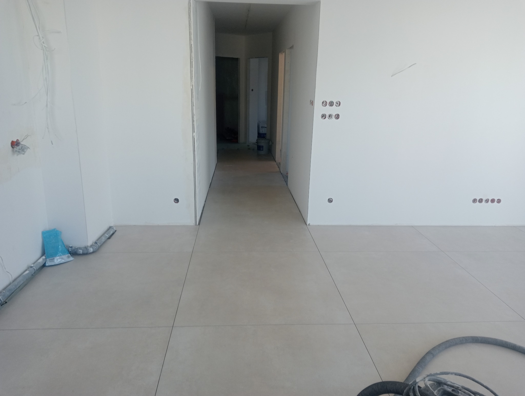 Wnętrze w stanie deweloperskim, świeżo po wylaniu posadzki, widoczne przygotowane instalacje elektryczne i rury wentylacyjne.