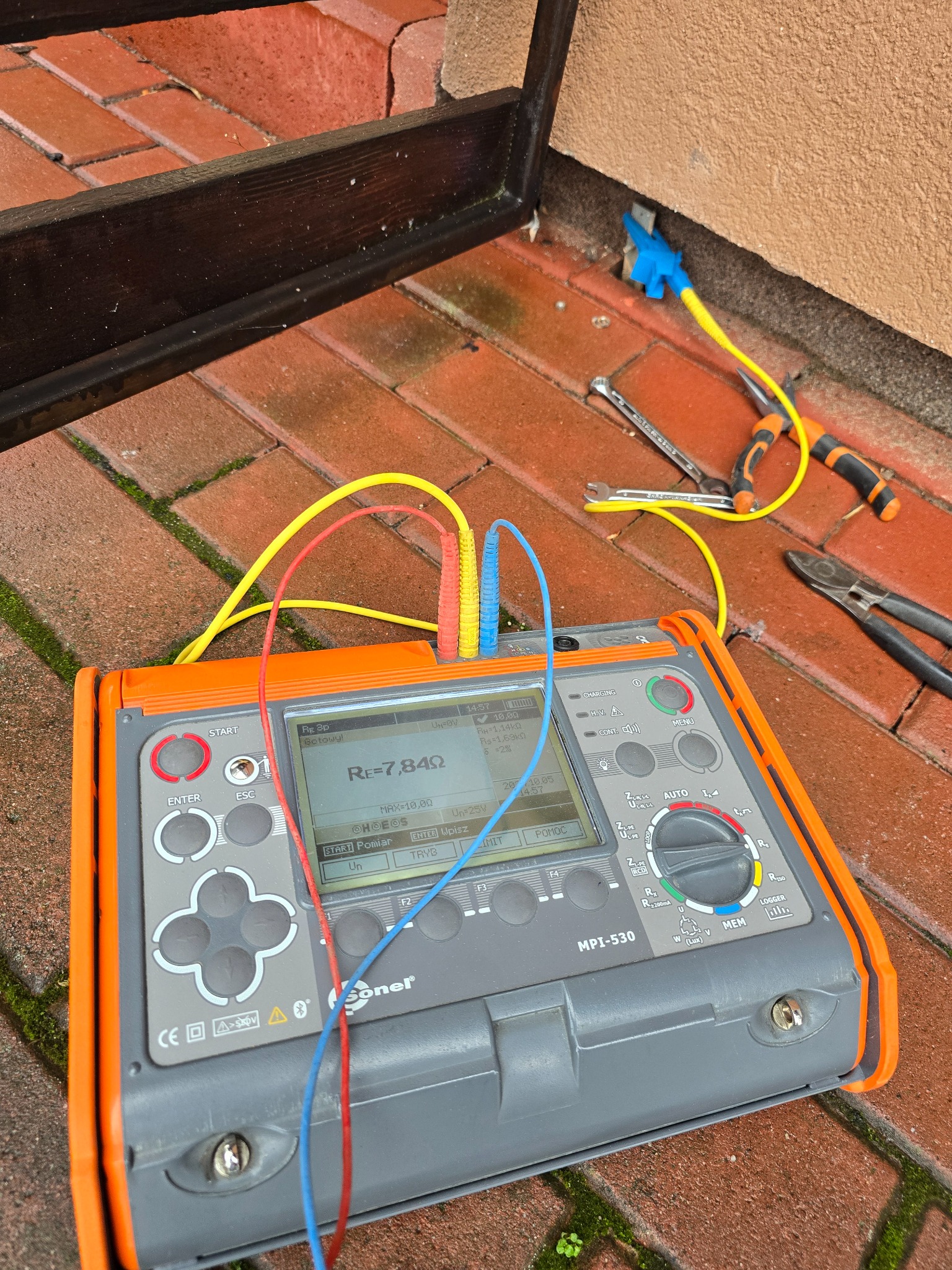 Miernik Sonel MPI-530 z podłączonymi przewodami pomiarowymi, pomiar rezystancji uziemienia przyłącza, obok leżą narzędzia: klucz płaski i szczypce