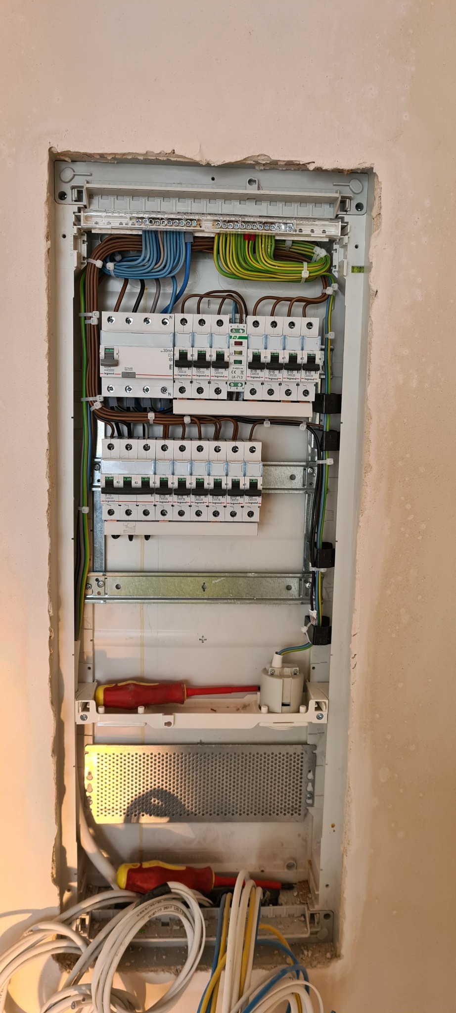 Rozdzielnica elektryczna w trakcie montażu w ścianie, widoczne kable, bezpieczniki i dwa śrubokręty.