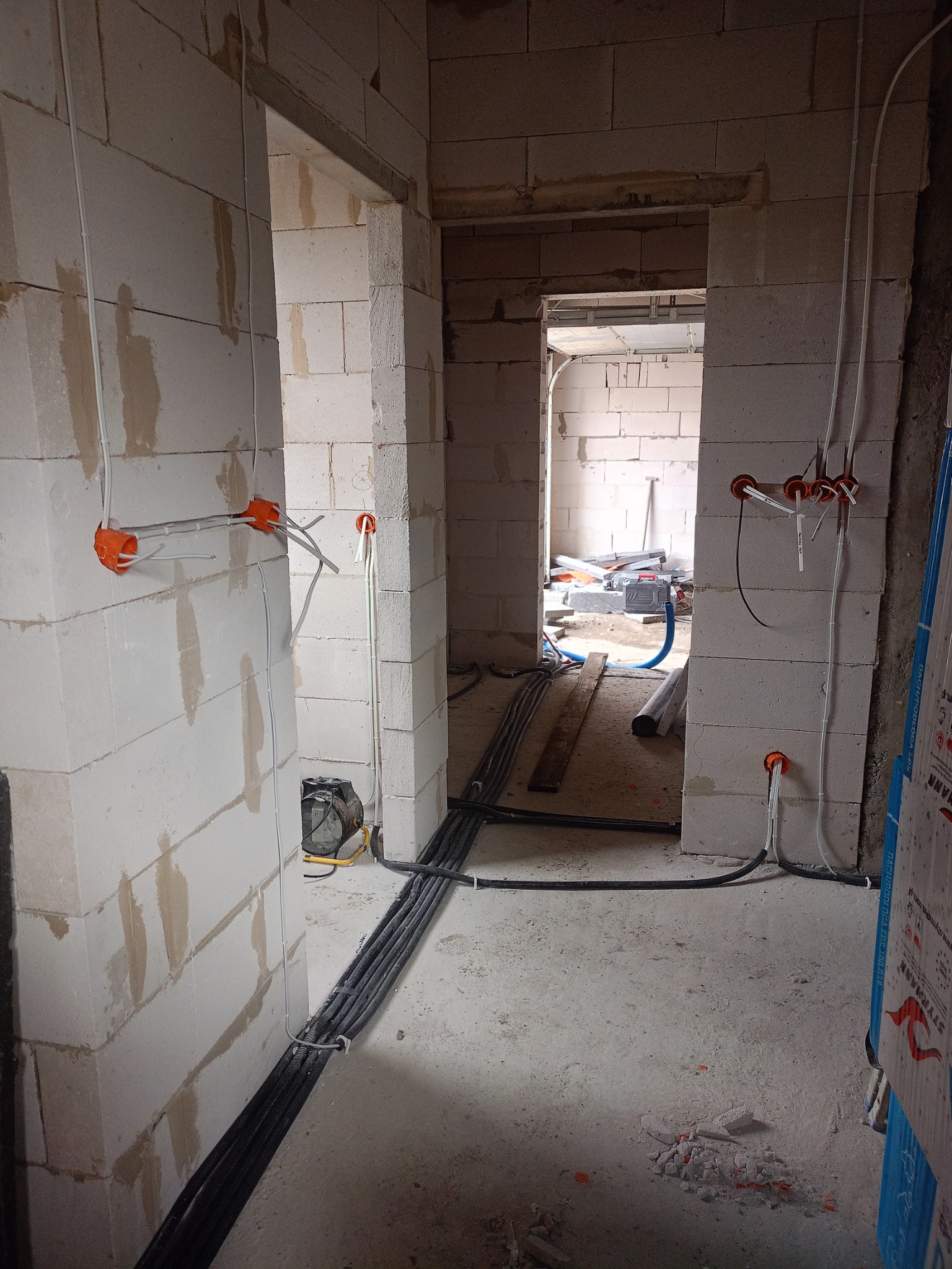 Surowy stan instalacji elektrycznej w nowym budynku: pomarańczowe puszki podtynkowe z wystającymi przewodami, kable w peszlach ułożone wzdłuż ściany z betonu komórkowego, widoczne narzędzia...