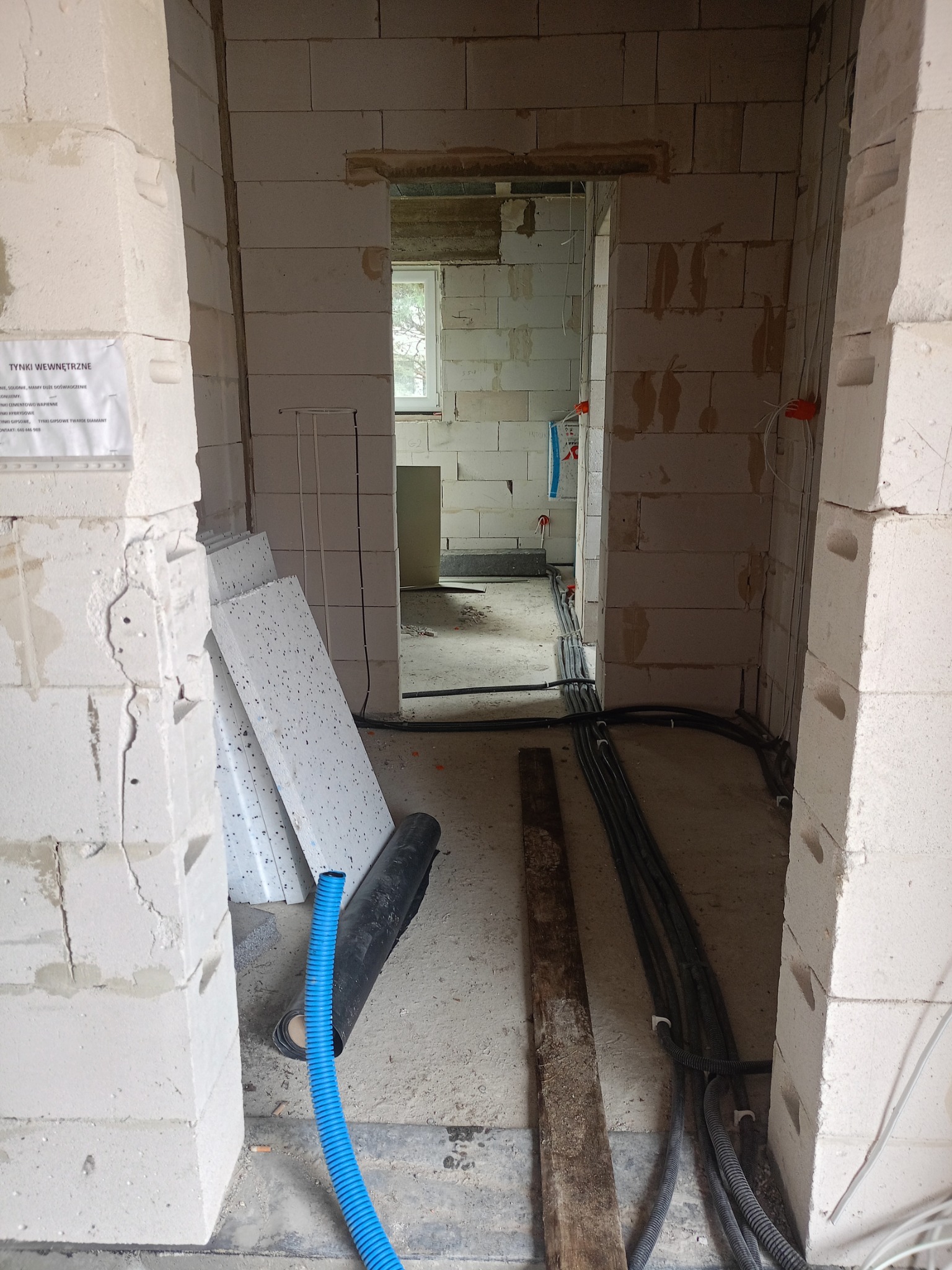 Surowy stan wnętrza w trakcie instalacji elektrycznej: widoczne przewody w peszlach, puszki elektryczne, ściany z betonu komórkowego, materiały budowlane i informacja o tynkach wewnętrznych...