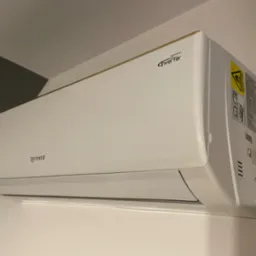 Biała jednostka wewnętrzna klimatyzatora Rotenso Inverter zamontowana na ścianie, widoczna z boku pod kątem, z naklejką ostrzegawczą i specyfikacją techniczną po prawej stronie.