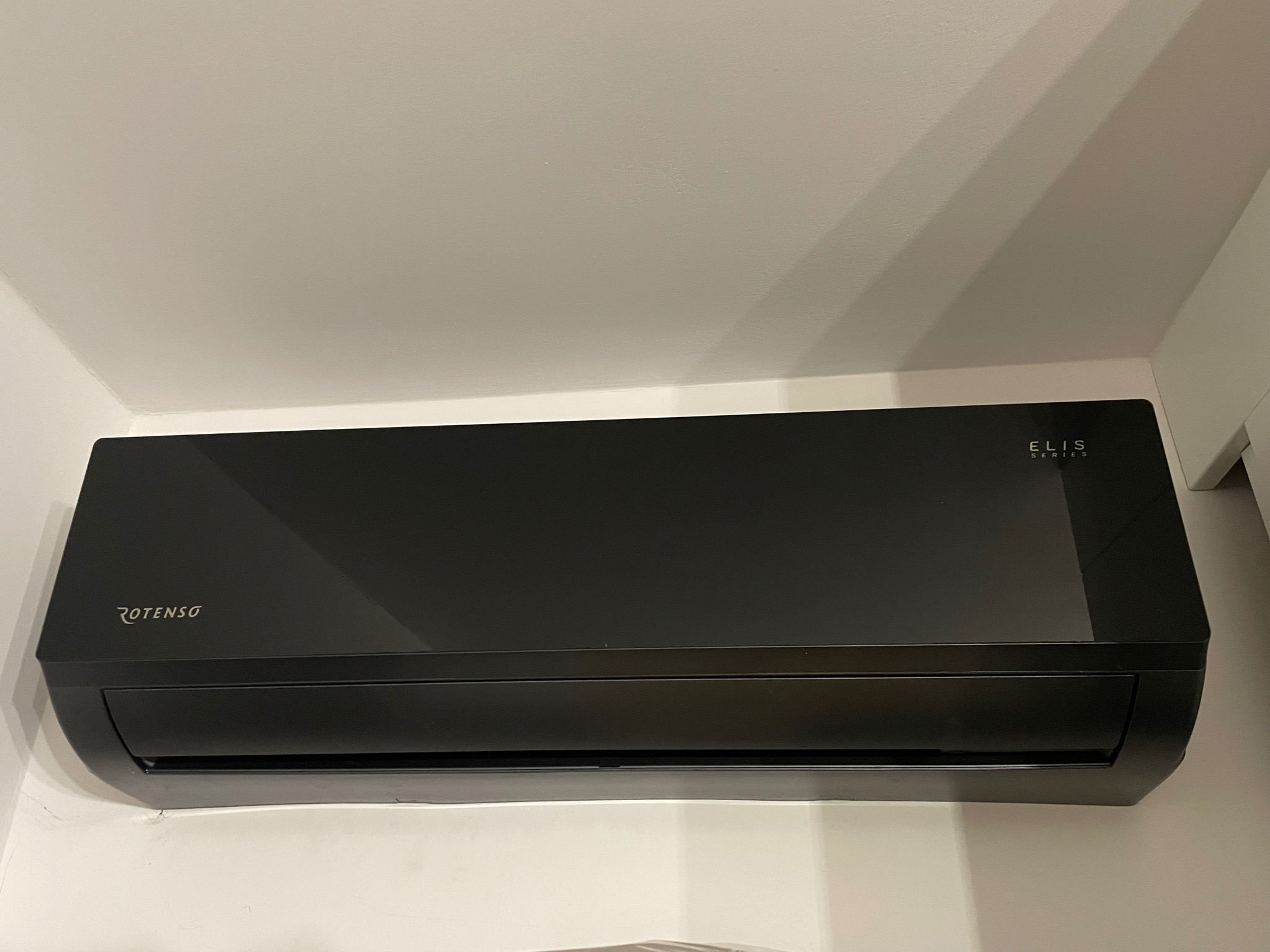 Czarny klimatyzator Rotenso Elis Series zamontowany na białej ścianie, widoczne niedoskonałości łączenia ściany i urządzenia.