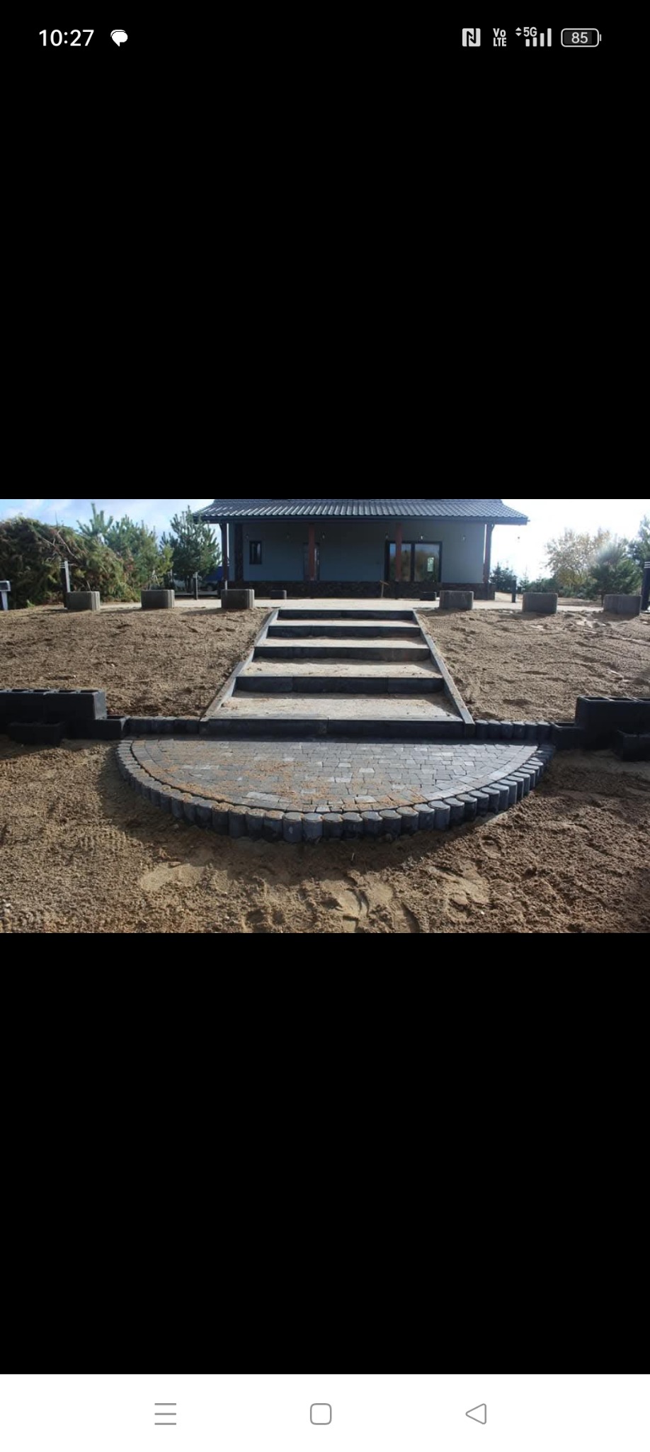 Półokrągły taras z kostki granitowej i schody prowadzące do domu, otoczone piaskiem.