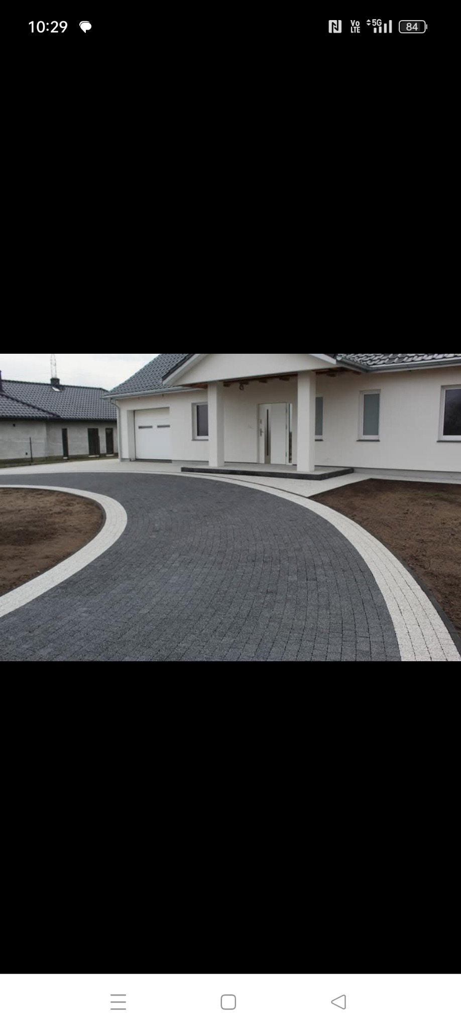 Nowoczesny dom z podjazdem wyłożonym szarą kostką z białymi obrzeżami ułożoną w łukowaty wzór.