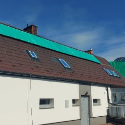Grzegorz Zabrzeński EKOPRO - Dom z brązowym dachem krytym zieloną plandeką. Widoczne okna dachowe i panele słoneczne. Przygotowanie do malowania dachu lub elewacji.