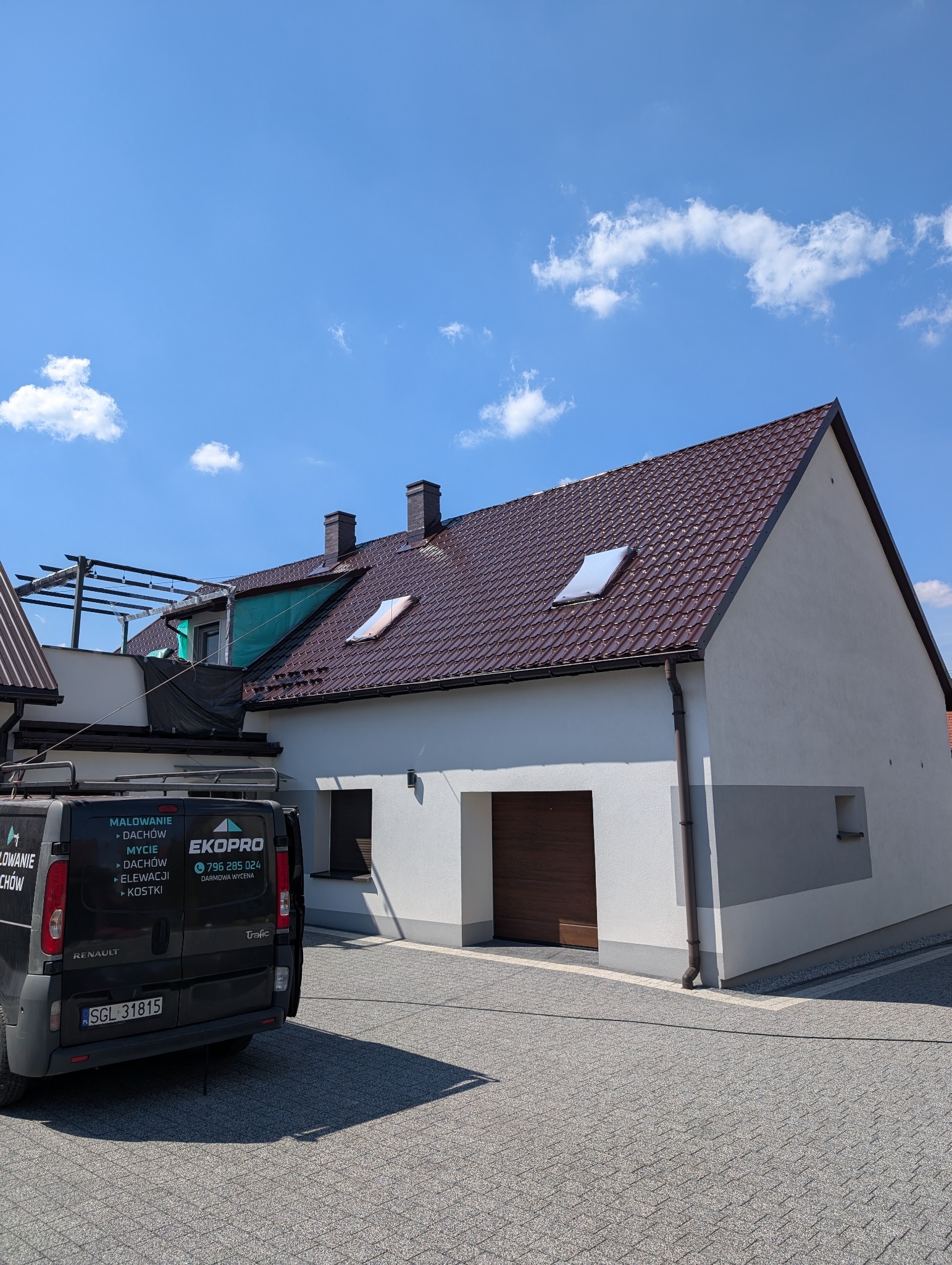 Dom po renowacji z nowym, brązowym dachem i jasną elewacją. Na podjeździe stoi firmowy van z reklamą usług malowania i mycia dachów oraz elewacji.