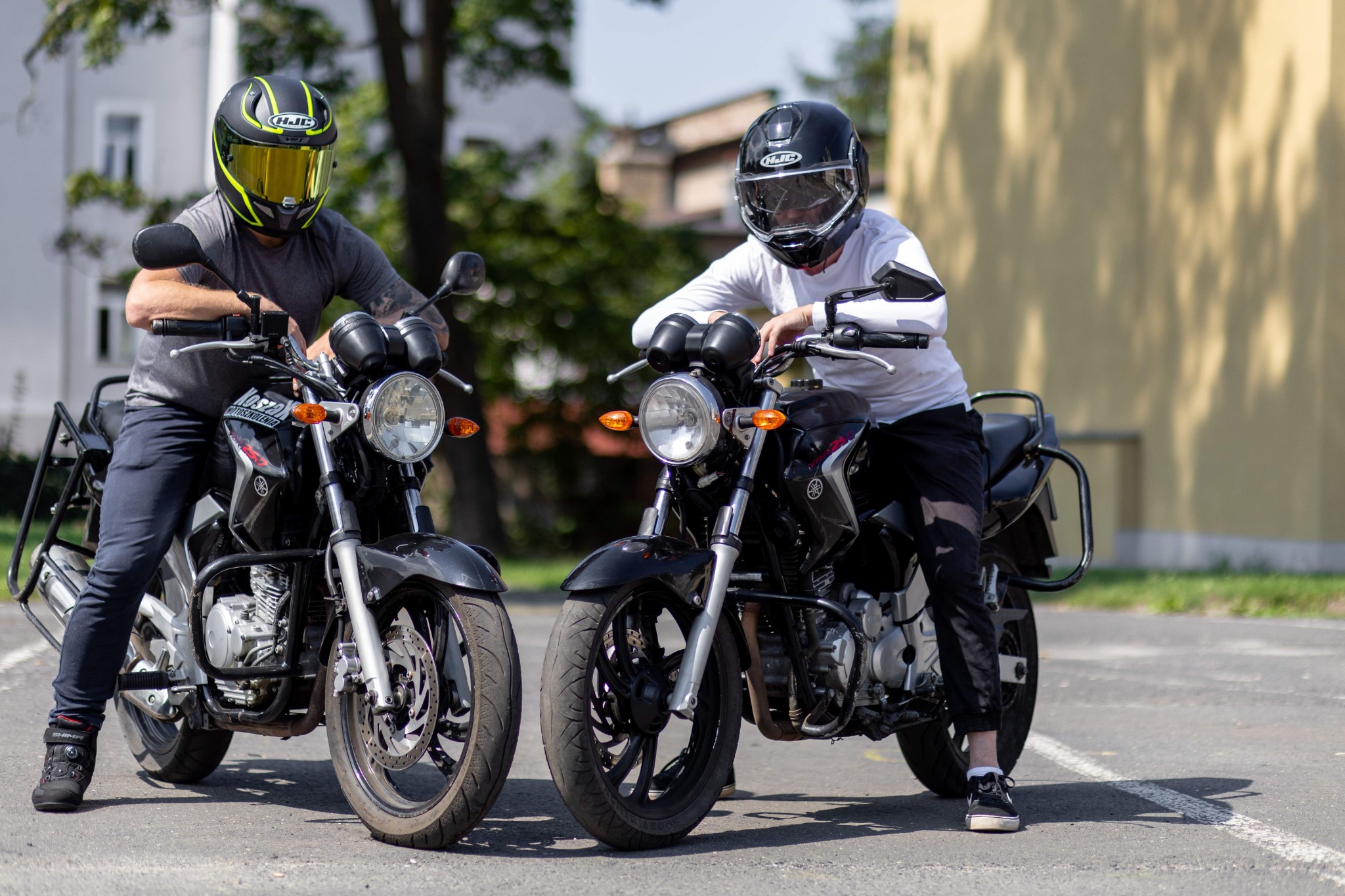 Dwaj kursanci w kaskach HJC siedzą na czarnych motocyklach Yamaha, przygotowując się do jazdy na placu manewrowym.