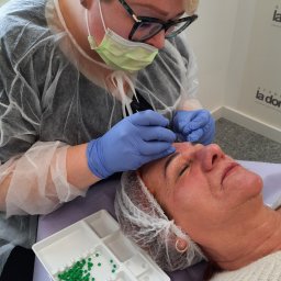 Harmonia Piękna Gabinet Kosmetyczny Karolina Kenkel - Zabieg medycyny estetycznej: aplikacja preparatu igłą w okolice brwi pacjentki leżącej na leżance, widoczne zielone kropki preparatu w pojemniku.