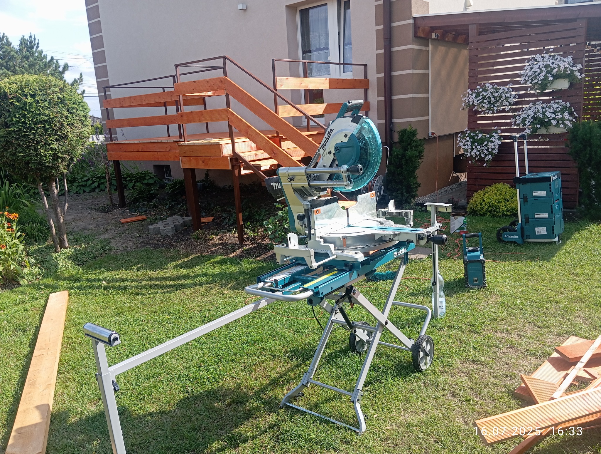 Budowa tarasu: ukończone schody z drewna prowadzą na podest. W tle maszyna do cięcia drewna marki Makita i skrzynka narzędziowa. Prace w ogrodzie.