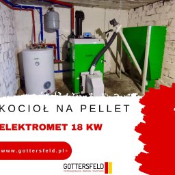 GOTTERSFELD SPÓŁKA Z OGRANICZONĄ ODPOWIEDZIALNOŚCIĄ - Kotłownia z kotłem na pellet Elektromet 18 kW, z widocznymi rurami instalacji grzewczej, zbiornikiem wyrównawczym i podajnikiem paliwa, zamontowana w piwnicy z surowymi ścianami.
