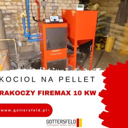 GOTTERSFELD SPÓŁKA Z OGRANICZONĄ ODPOWIEDZIALNOŚCIĄ - Kocioł na pellet Rakoczy Firemax 10 kW, widoczne orurowanie instalacji grzewczej, tło z ceglaną ścianą. Na kotle panel sterowania.