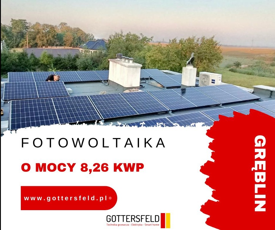 Instalacja paneli fotowoltaicznych na płaskim dachu budynku, widok z góry, z widoczną sylwetką instalatora podczas pracy, w tle drzewa i budynki.