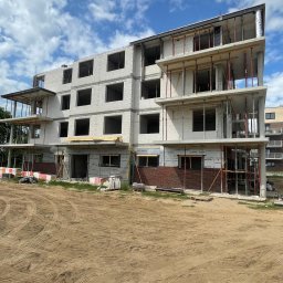 DD FIRMA USŁUGOWO-BUDOWLANA - Trzykondygnacyjny budynek w stanie surowym otwartym z widocznymi elementami szalunków, ceglaną elewacją na parterze i przygotowanym terenem pod budowę.