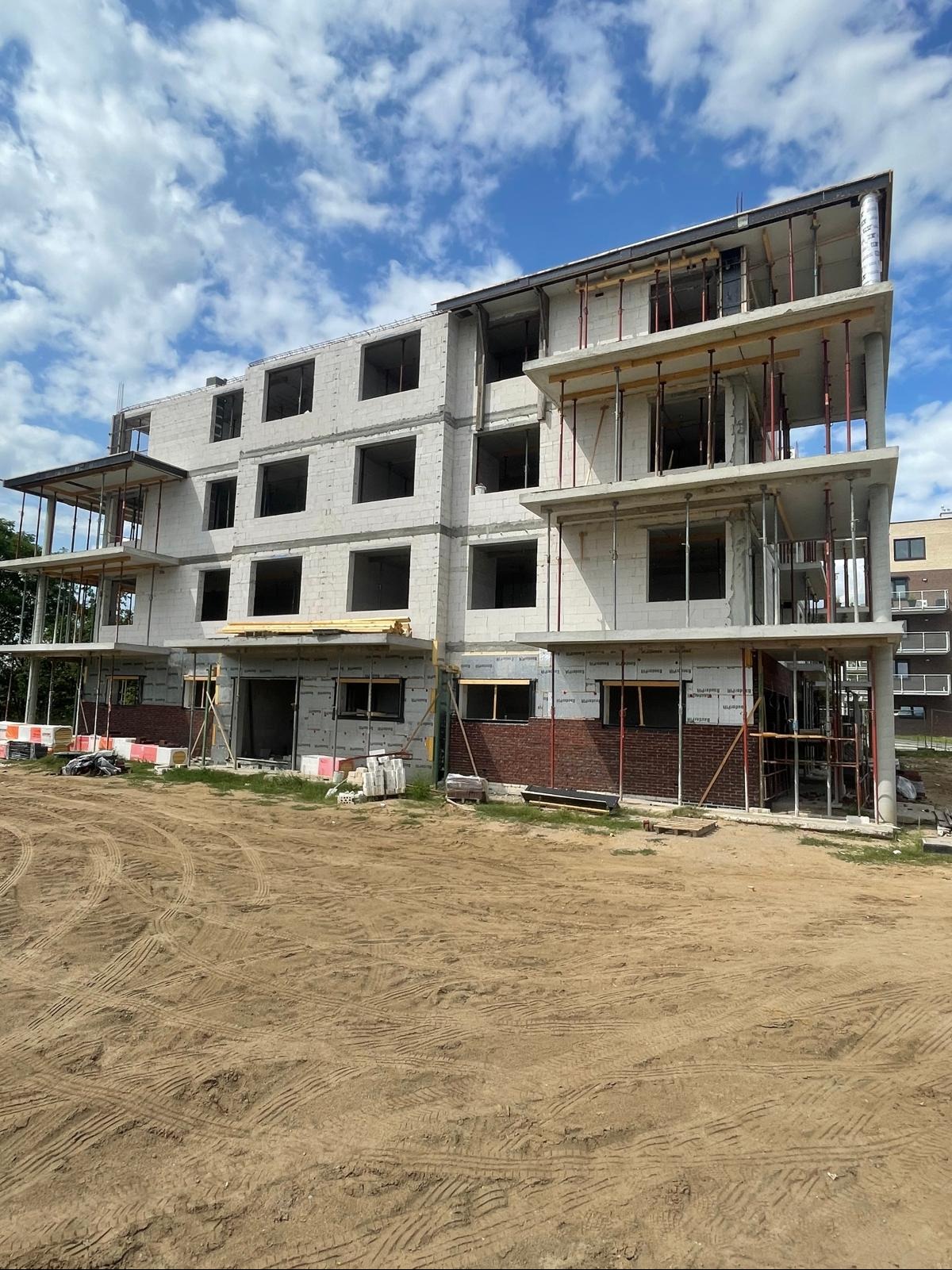 Trzykondygnacyjny budynek w stanie surowym otwartym z widocznymi elementami szalunków, ceglaną elewacją na parterze i przygotowanym terenem pod budowę.
